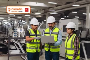 ERP para Manufactura. Equipo de supervisores y operarios con casco y chaleco de seguridad revisando información en una laptop dentro de una planta de manufactura industrial.